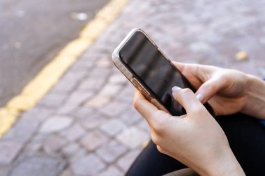 Rahat bir kızın ellerini yakın, bir caddede otururken cep telefonunu kontrol edin.