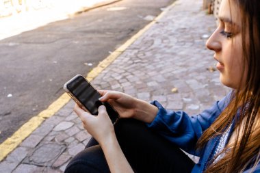 Rahat bir kızın telefonunu kontrol edip caddede otururken yakın plan fotoğrafını çek.