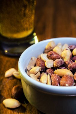 Bir bardak bira, masada fıstık ve ahşap bir masada beyaz bir kâse..