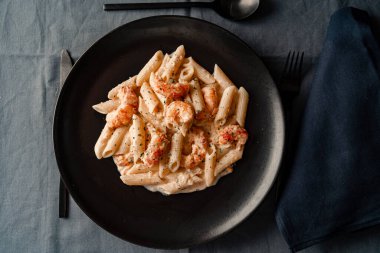 Kuru makarna ve nefis karides ve karides kremalı siyah bir tabak manzarası..