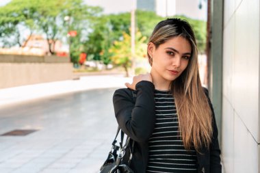 Güneşli bir günde bir ofis binasının duvarında ciddi bir ifadeyle duran güzel girişimci kadın..