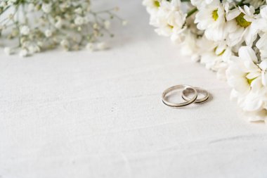 Beyaz bir yüzeyde güzel beyaz çiçekli bir çift alyans. Bağlılık ve aşk kavramı. Boşluğu kopyala, diferansiyel odak.