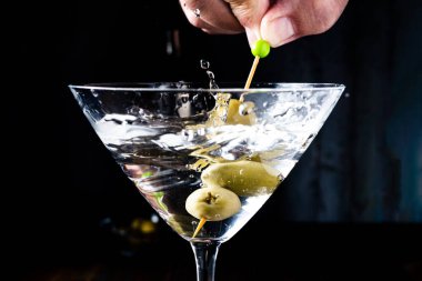 a Hand removing some olives from a classic conical martini glass and generating splashes. Horizontal orientation.