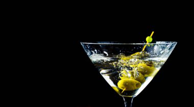 Elegant dry martini glass with olives splashing on black background and copy space. Horizontal orientation.