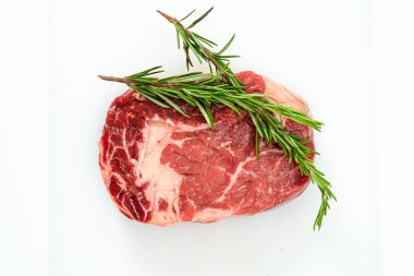 Beyaz bir yüzeye çiğ pirzola bifteği ve birkaç tutam taze biberiye. Yemek konsepti. Genel Görünüm.