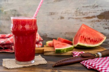 Büyük bardakta soğuk karpuz püresi ve arka planda lezzetli karpuz üçgenleri. Sağlıklı, taze ve doğal bir içecek. Mevsim meyveleri.