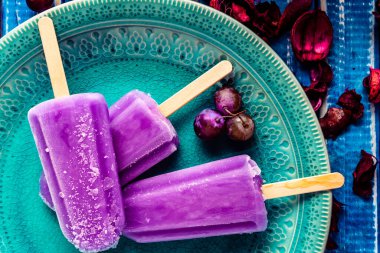 Lolipop stili üzümlü dondurma, açık mavi ahşap bir masada klasik bir tabakta. Doğal ve sağlıklı beslenme kavramı.