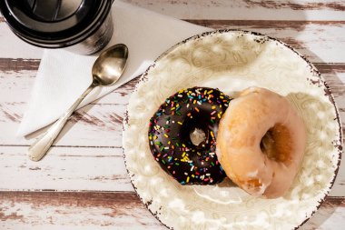 İki ev yapımı donutun havadan görünüşü. Çikolata, çikolata serpintisi ve ahşap bir masanın üzerindeki bir tabakta kraliyet kreması. Boşluğu kopyala.