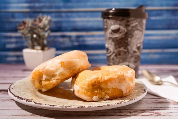 Eski ahşap bir masanın üzerinde kahve olan bir bardağın yanında, antika bir tabakta kremayla kaplı iki ev yapımı çörek. Yüksek görüş, yatay uyum. Ev yapımı kahvaltı..