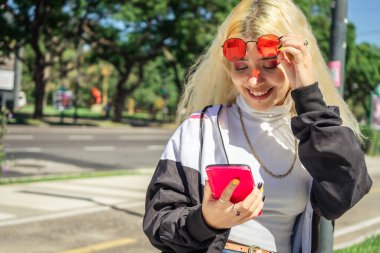 Genç Latin kadın akıllı telefonundaki mesajları kontrol ediyor. Parktaki bankta oturuyor. Teknoloji ve telekomünikasyon kavramı, modern kadın.