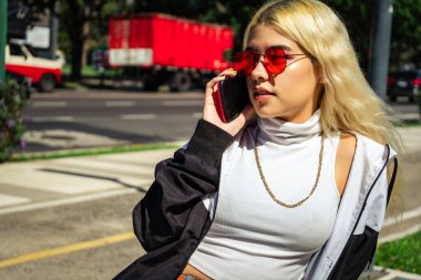 Genç Latin bir kadın akıllı telefonuyla parktaki bankta oturuyor. Teknoloji ve telekomünikasyon kavramı, modern kadın. Boşluğu kopyala.