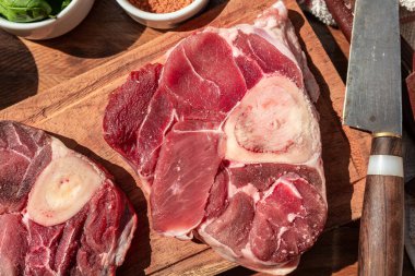 Tahtada taze çiğ ossobuco bifteği ve ahşap bir masada süslemeler. Hayvan proteini konsepti, İtalyan yemeği. Aereal görünüm