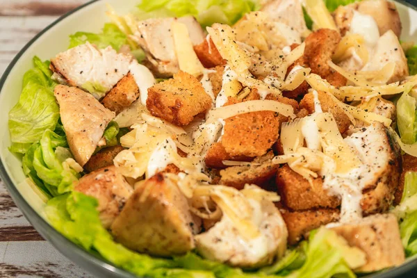 Exquisite Caesar salad with small bites of chicken and a traditional aioli sauce in a small bowl on a rustic table. High view. Close-up detail.