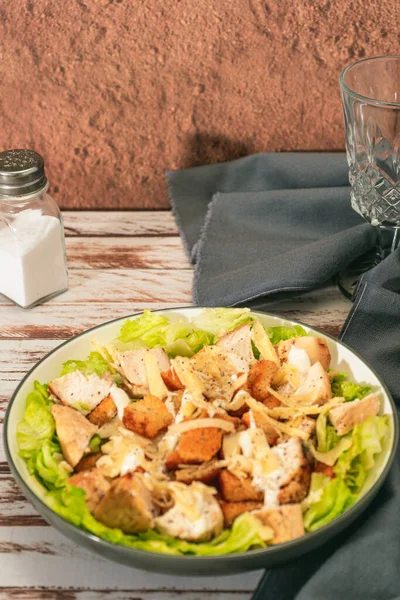 Exquisite Caesar salad with small bites of chicken and a traditional aioli sauce in a small bowl on a rustic table. High view. Vertical orientation.