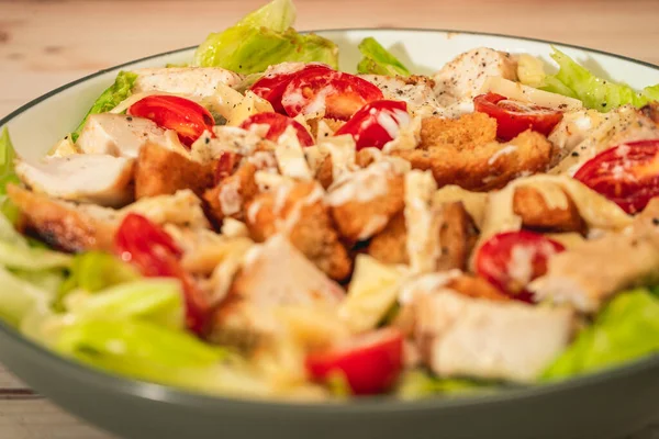 Variation of Caesar salad with small bites of chicken, cherry tomatoes and a gourmet aioli sauce in a small bowl on a rustic table. High view. Close-up detail.