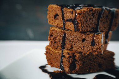 Çikolatalı Brownie yığınının beyaz bir tabağa ve siyah bir arka plana düşen çikolata telli yakın çekimi. Normal görünüm.