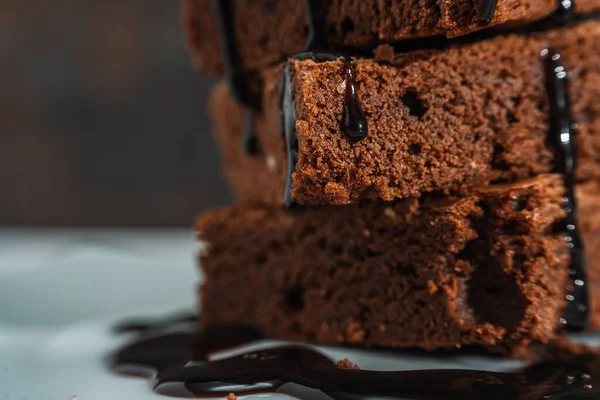 Çikolatalı Brownie yığınının beyaz bir tabağa ve siyah bir arka plana düşen çikolata telli yakın çekimi. Normal görünüm.