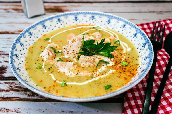 Exquisite dish with a homemade cream of poultry soup with chicken pieces, parsley and cream on a rustic or country style wooden table. Natural and simple food concept.