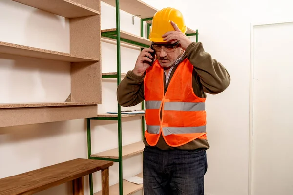 Mature Caucasian inspector talking on cell phone while checking the status and progress of the work in the work office. Concept of labor organization, inspecting, Telecomunications.