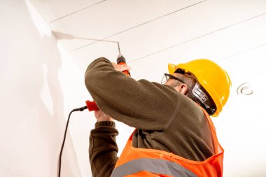 Operator dressed in safety uniform like vest, helmet and safety glasses, drilling a roof with a drill. Concept of work, builder, worker.