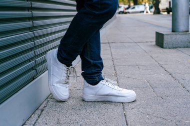 Feet of unrecognizable man leaning on a front of a modern building on a sunny day. Copyspace.
