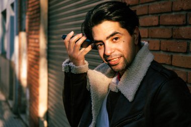 A Latin young man listening to a message on his cell phone in the street. Concept of communications, technology, IT.