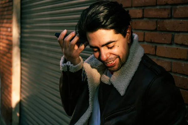 A Latin young man listening to a message on his cell phone in the street. Concept of communications, technology, IT.
