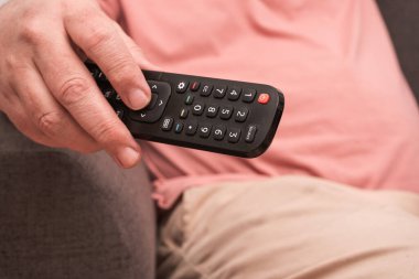 unrecognizable man sitting on a sofa with a remote control in his hand changing channels on the television. concept of rest and relaxation
