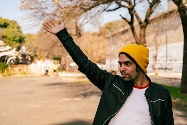 Молодой Латиноамериканец Жёлтой Шерстяной Шапочке Приветствует Другого Человека Поднятой Рукой — стоковое фото
