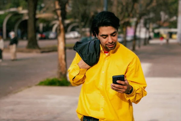 A young Latino man checking messages on his cell phone as he walks down a street