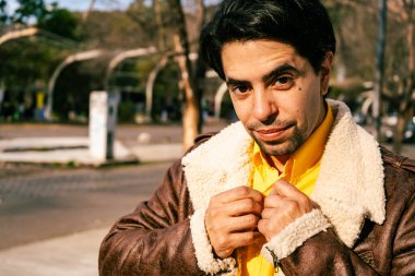 A portrait of a handsome young latino man walking alone down a street on a sunny day