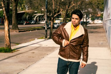 A portrait of a handsome young latino man walking alone down a street on a sunny day