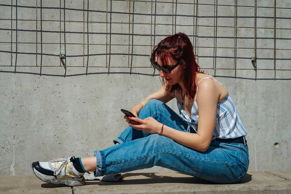 一位漂亮的红头发拉丁女人舒服地坐在长椅上检查她的手机 复制空间 景观定位 — 图库照片
