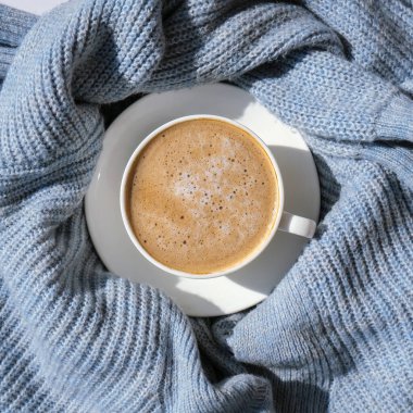 Mavi süveter üzerine beyaz bir fincan sabah kahvesi. Sıcak ev sonbahar konsepti. Estetik blog yaşam tarzı. Hayat konsepti. Cappuccino ya da latte sıcak içecek. Üst görünüm düzlüğü