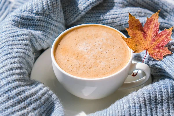 Akçaağaç sarısı yapraklı mavi örgü süveterin üzerinde beyaz bir sabah kahvesi. Konforlu ev konsepti. Estetik blog yaşam tarzı. Sonbahar sakin bir hayat. Cappuccino ya da latte sıcak içecek. Atmosfer