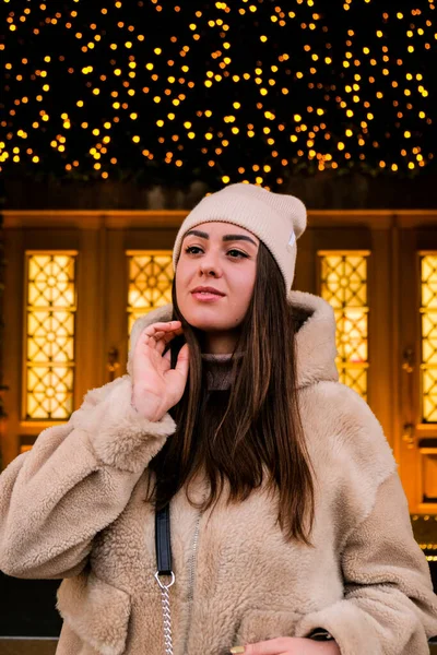 若い美しい女性が新年の装飾された通りの市場の屋外で歩く 伝統的なクリスマスマーケットの雰囲気 ボケの光を持つ若い女性の肖像画 クリスマスの装飾都市の通りを背景に — ストック写真