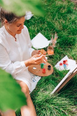Bahçedeki sehpada ressam resmi. Açık hava sanat atölyesi. Parktaki bir piknik sırasında çimlerin üzerine fırça ve paletle resim çiz.