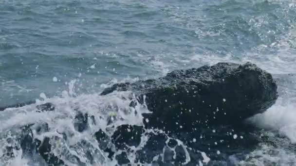 Waves break on rocks in blue ocean. Sea ocean waves crashing against an empty stone rock cliff. Crashing at rocky cliff with splashing and white foam. — Stock Video