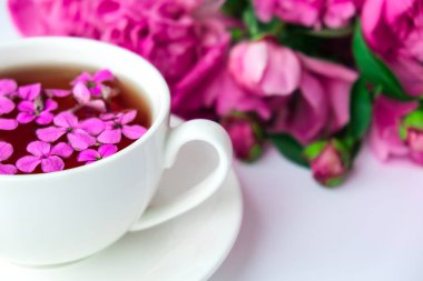 Pembe şakayık çiçekleri ve parlak masa üzerinde bir fincan çayla yaratıcı bir düzen. Bahar mevsimi sevgililer günü, kadın, anne, 8 Mart bayramı, romantik kahvaltı. Şık bir blog yazarı. Tebrik kartı. Davetiye. Günlük postası