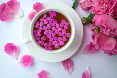 Pembe şakayık çiçekleri ve parlak masa üzerinde bir fincan çayla yaratıcı bir düzen. Bahar mevsimi sevgililer günü, kadın, anne, 8 Mart bayramı, romantik kahvaltı. Şık bir blog yazarı. Tebrik kartı. Davetiye. Günlük postası