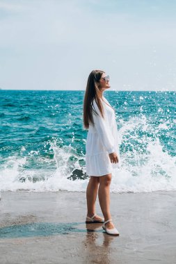 Plajda gökyüzüne karşı poz verirken giyinen ve su sıçratan bir kadın. Deniz manzaralı. Yaz tatili konsepti. Kumsalda bir günün tadını çıkarıyorum.