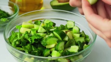 Taze yeşil sebze ve ottan salata pişiren bir kadın. Çiğ gıda konsepti. Vejetaryen menüsü. Sağlıklı beslenme ya da vejetaryen yemekleri pişirmek. Dişi eller kesme tahtasındaki salatalıkları kesiyor.