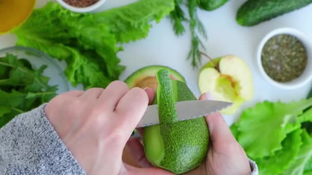 Donna che cucina insalata di verdure verdi fresche ed erbe. Concetto di cibo crudo. Menù vegano. Cucina dieta sana o cibo vegetariano. Mani femminili tagliate avocado sul tagliere circondato da verdure verdi — Video Stock