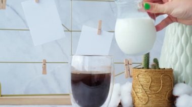 Kadın bir fincan kahveye süt ekliyor. Ağır çekim Beyaz ofis içi iç mekan, blog yazarlarının işyeri. Kartpostallı ve hatırlatıcı maketli bir ruh hâli. Vazoda pamuk dallar, iç dekorasyon.