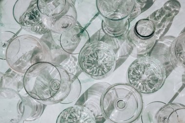 Güneş ışığında beyaz arka planda duran farklı güzel gözlükler gölgeler yaratır. Sert ışık, uzun gölgeler. Yaratıcı içki konsepti, alkol kokteyli. Cam kaplama konsepti. Geometrik şekiller