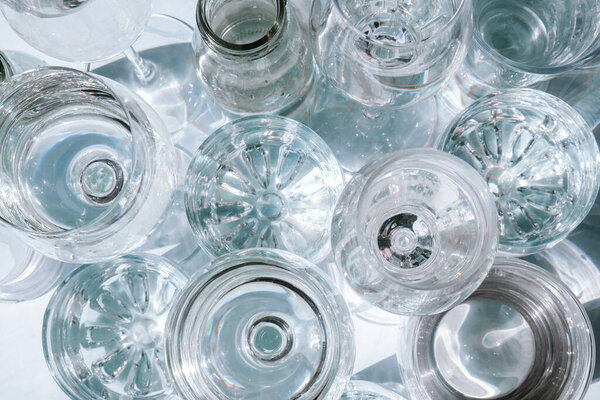 Beautiful different glasses stand on white background in sunlight and create shadows. Hard light, long shadows. Creative concept of drinks, alcohol cocktails. Glassware concept. Geometric shapes