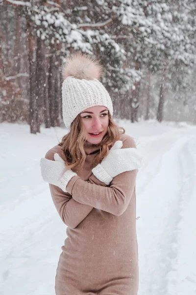 Vánoce, svátky a sezónní koncept. Mladá šťastná žena fouká sníh v zimním lese přírody. Teplé oděvy pletené rukavice a klobouk. — Stock fotografie
