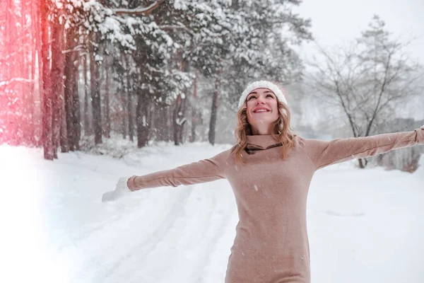 Christmas, holidays and season concept. Young happy woman blowing snow in the winter forest nature. Warm clothing knitted gloves and hat. — Stock Photo, Image