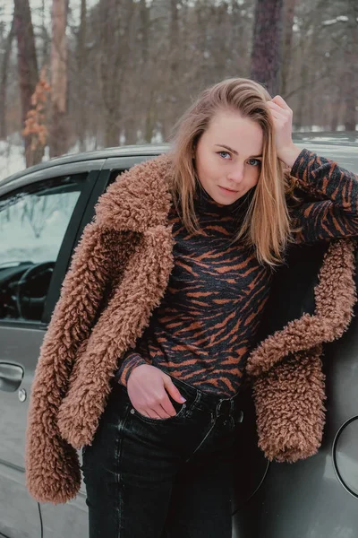 Atractiva hermosa mujer joven en suéter que se aloja al lado del coche en el bosque. Vacaciones de invierno. Vacaciones. Molienda —  Fotos de Stock