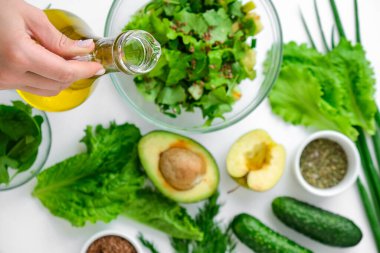 Taze yeşil sebze ve ottan salata pişiren bir kadın. Sağlıklı beslenme ya da vejetaryen yemekleri pişirmek. Kadın elleri zeytin yağı ekler. Adım adım tarif et. Sağlıklı beslenme. Salata için malzemeler. Sağlıklı vejetaryen yemek malzemeleriyle düz bir şekilde yatıyordu. Çiğ.
